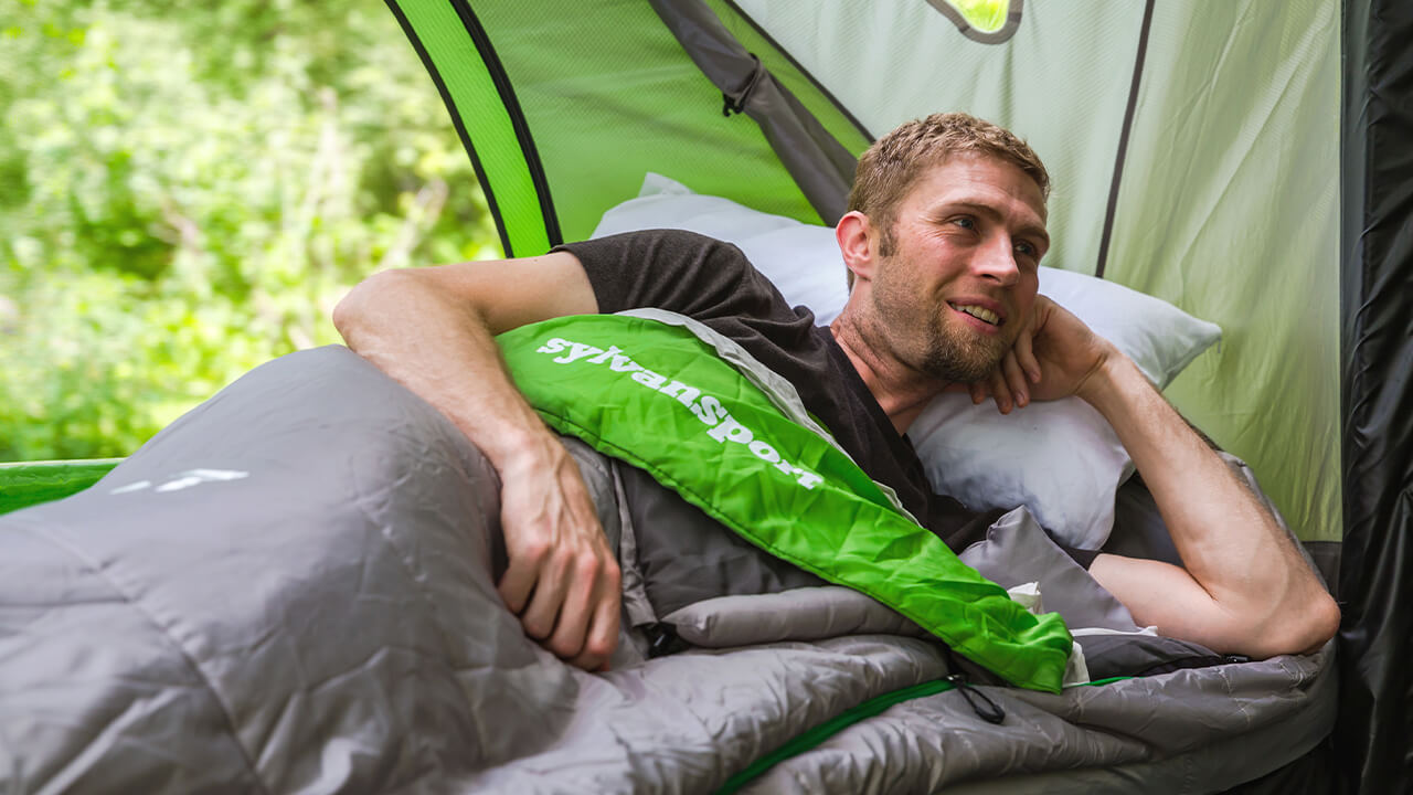 man laying on side in sleeping bag in GO camping trailer