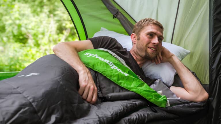 A man relaxing inside a SylvanSport Optima camping trailer with a green and black interior.
