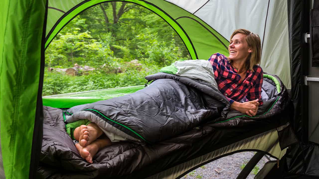 A woman relaxing inside a SylvanSport camping tent in a lush green forest.