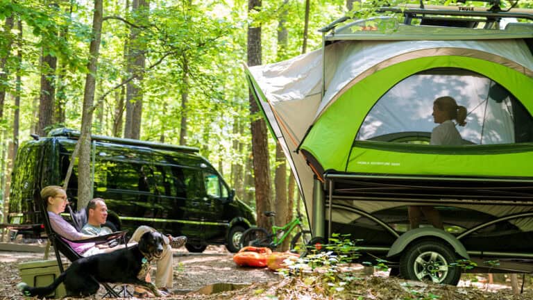 Optima camping trailer with tent setup in forest.