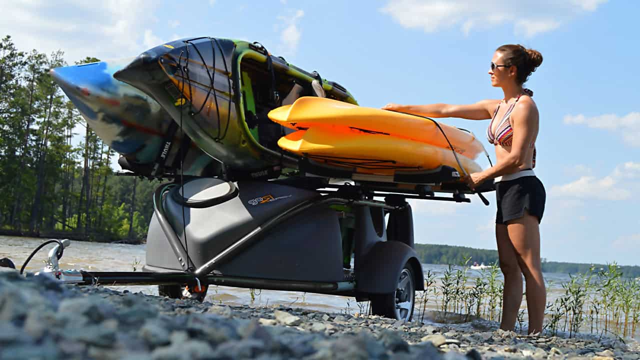 Woman loading kayak onto SylvanSport trailer by the lake.