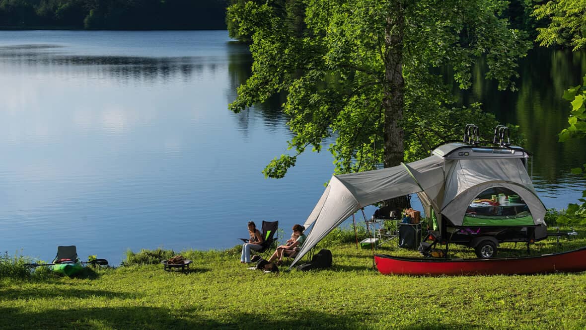 SylvanSport camping trailer at Canoecopia, with a tent extension and kayak nearby, perfect for outdo.