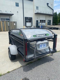 SylvanSport trailer with black frame and clear canopy for outdoor gear transport.
