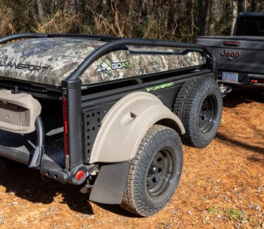 Compact SylvanSport camping trailer with rugged off-road tires on a dirt trail.
