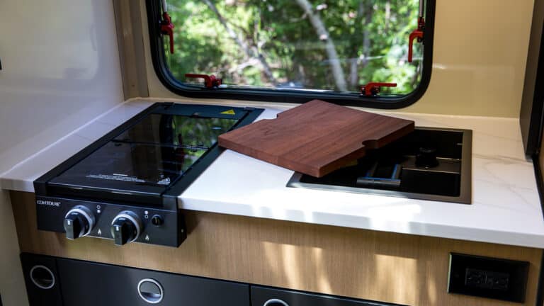 Compact kitchen area inside SylvanSport VIRE travel trailer with stove and cutting board.