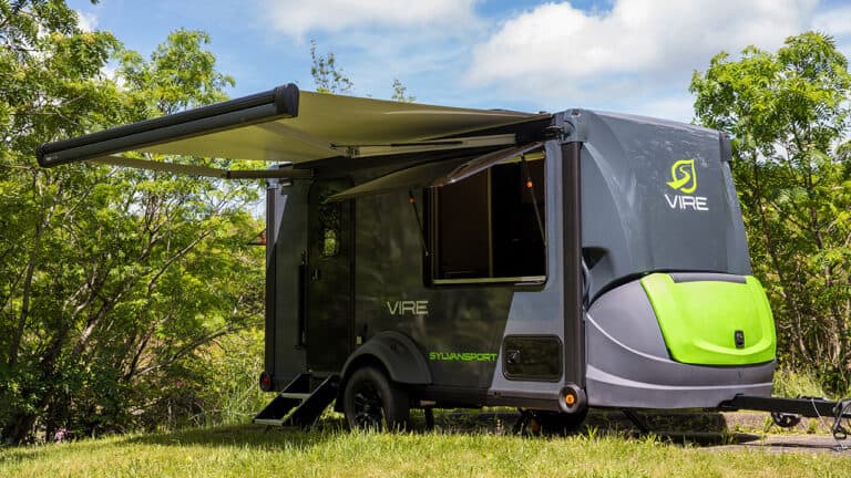 SylvanSport VIRE travel trailer with awning in a green outdoor setting.