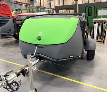 Green and gray SylvanSport trailer in industrial warehouse setting.