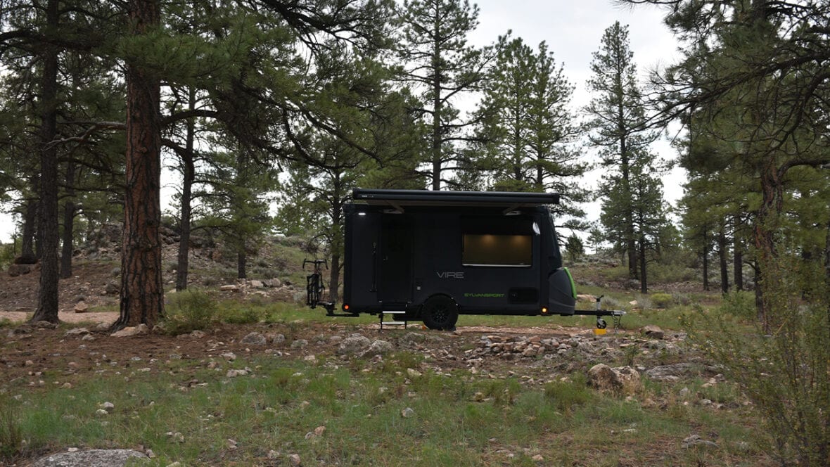 SylvanSport GO camping trailer in forest setting with trees and rocks.