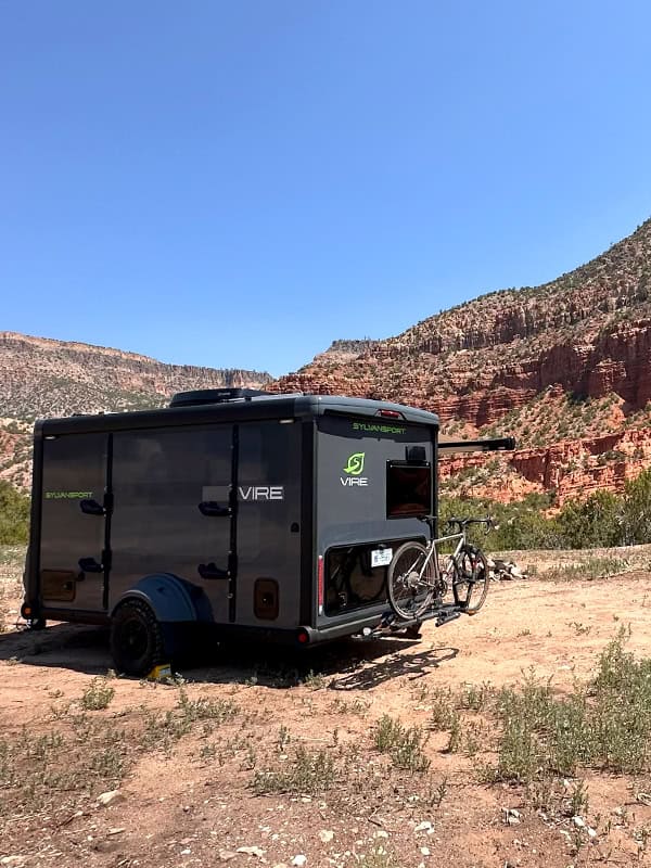 SylvanSport VIRE travel trailer with bike rack in desert landscape.