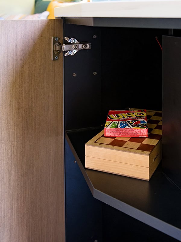 Inside a compact storage cabinet with a UNO game box and wooden block.