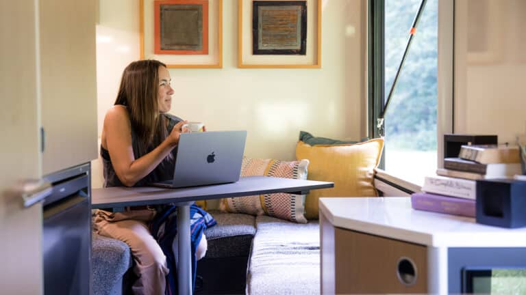 Woman working on a laptop in a cozy home office with large window and colorful artwork.