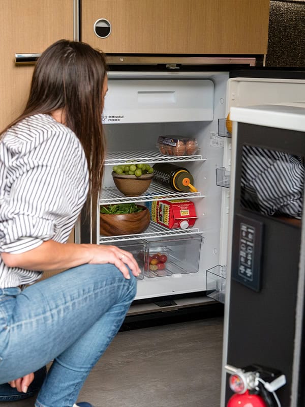 Woman opening refrigerator in a modern kitchen with food inside.