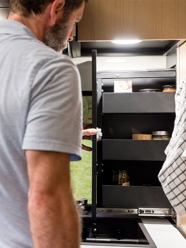 Man opening a compact kitchen cabinet in a SylvanSport VIRE Travel Trailer.
