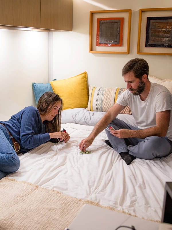 Couple relaxing inside SylvanSport VIRE travel trailer with cozy bedding and artwork.