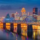Louisville skyline illuminated with city lights over the Ohio River at night.