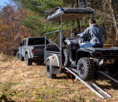 SylvanSport Optima trailer hauling ATV in outdoor terrain.